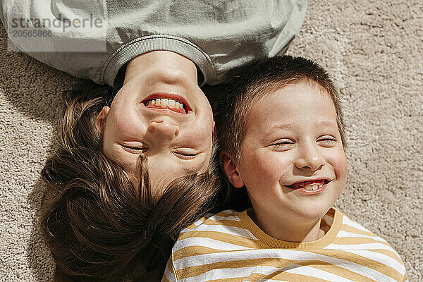 Cheerful siblings lying on carpet in living room at home