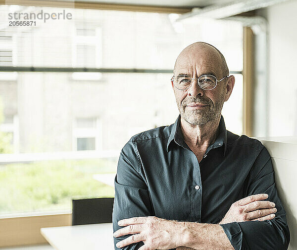 Confident mature businessman wearing eyeglasses with arms crossed standing in office