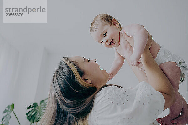 Happy young mother holding baby aloft at home