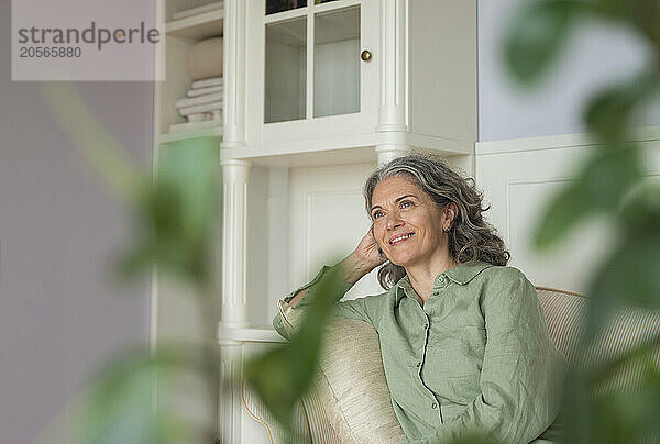 Smiling mature woman leaning on sofa at home