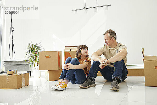 Daughter and father sitting amidst cardboard boxes in new house