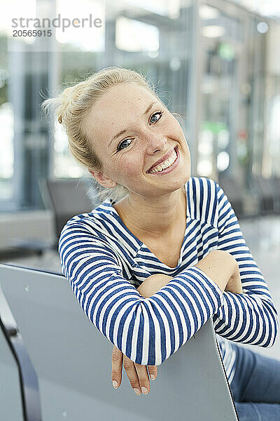 Happy young businesswoman sitting in airport lobby