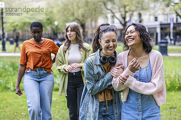 Cheerful women talking and walking in front of friends at park