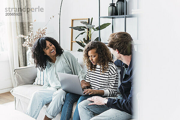 Laughing parents sitting on sofa with daughter using laptop