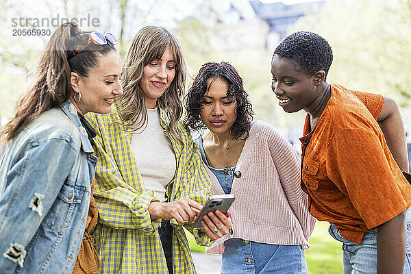 Smiling young woman sharing smart phone with friends at park