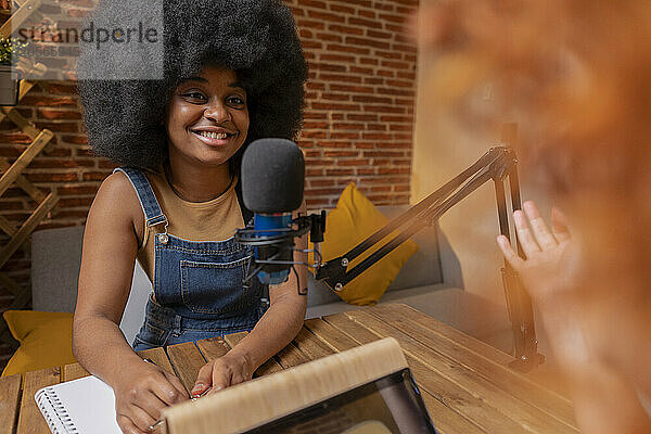 Smiling Afro woman recording podcast with friend at home