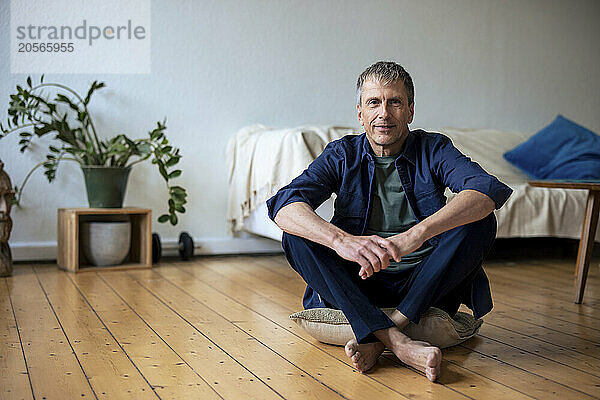 Smiling retired man sitting on cushion in living room at home