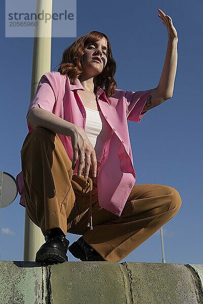 Confident redhead woman squatting and shielding eyes on sunny day