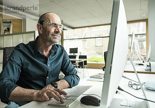 Smiling businessman wearing smart glasses using computer in office