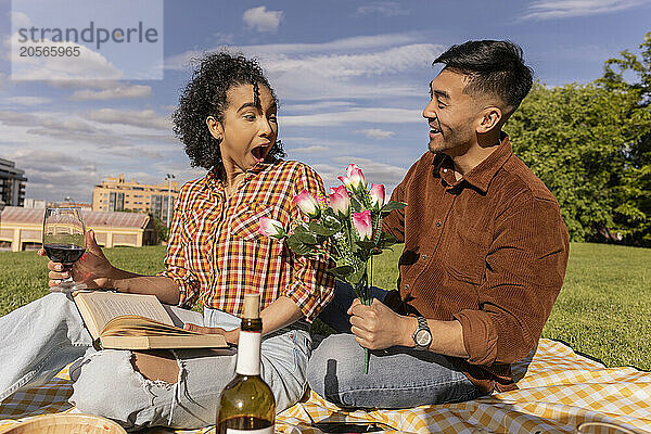 Shocked woman sitting with boyfriend holding flowers at public park