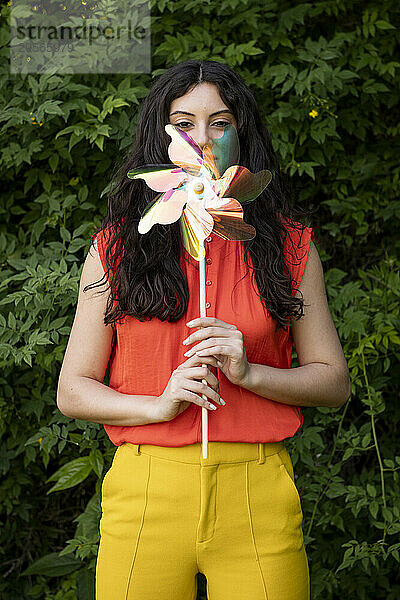 Beautiful woman covering face with pinwheel toy at garden