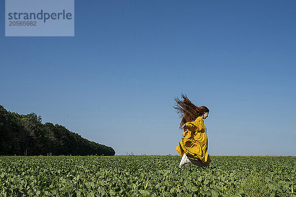 Teenage girl with red hair in a yellow dress running in a green field