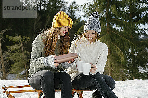 Happy woman pouring coffee in mugs enjoying winter vacation with friend