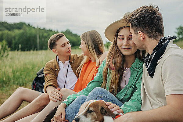 Group of affectionate young couples sitting with dog on mountain