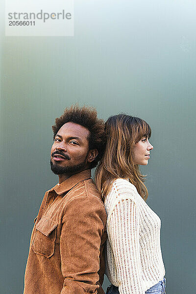 Confident man standing back to back with girlfriend against gray background