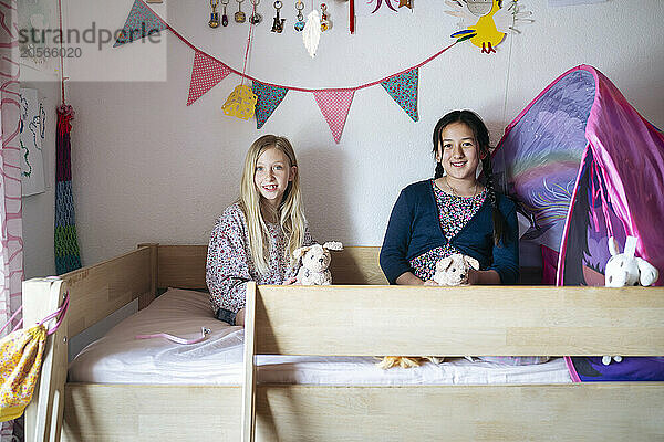 Happy multiracial girls playing together on bunk bed in bedroom at home