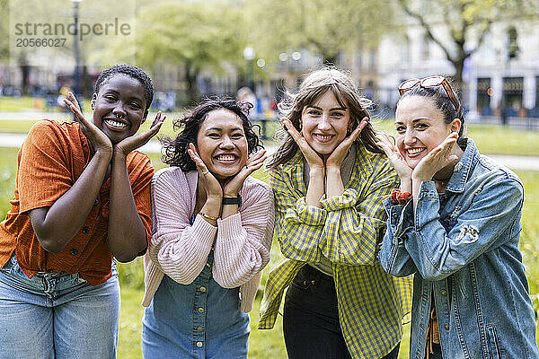 Cheerful female friends with heads in hands standing side by side at park