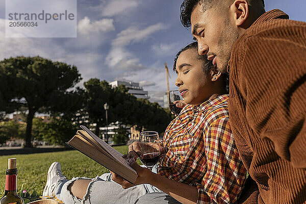 Multiracial couple reading book at public park