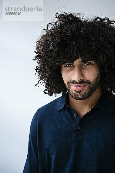 Confident businessman with curly hair in front of white wall