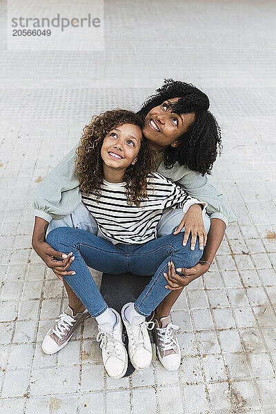 Mother and daughter sitting on skateboard looking up