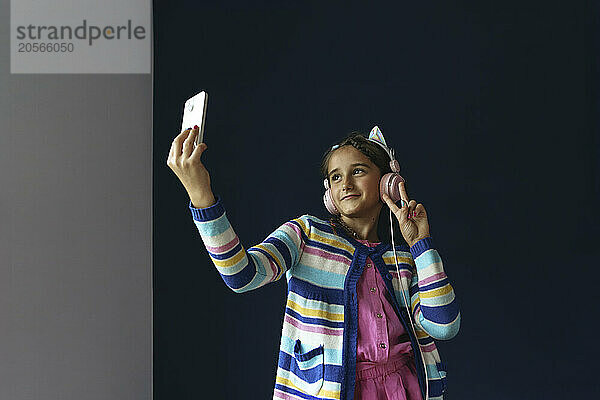 Smiling girl taking selfie through mobile phone at home