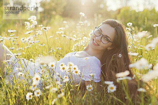 Smiling woman with long hair lying down amidst flowers in chamomile field