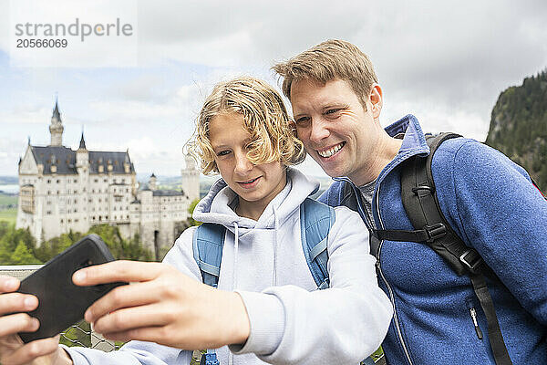 Son taking selfie with father through smart phone in front of a castle