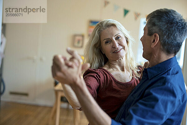 Smiling senior couple holding hands and dancing at home