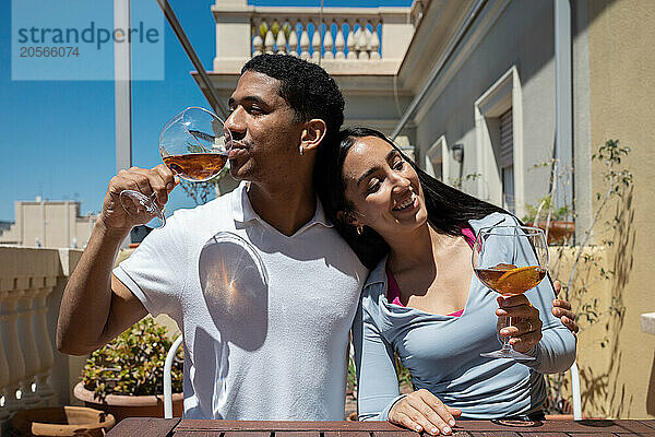 Smiling young woman leaning head on boyfriend drinking at rooftop