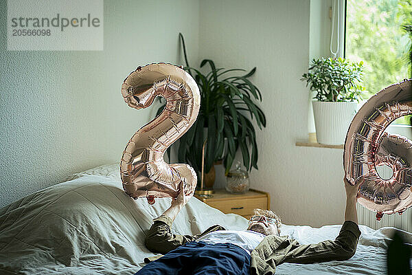 Depressed young man with number balloons lying on bed at home