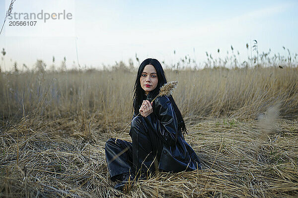 Beautiful woman sitting and holding crop plant in reeds at field