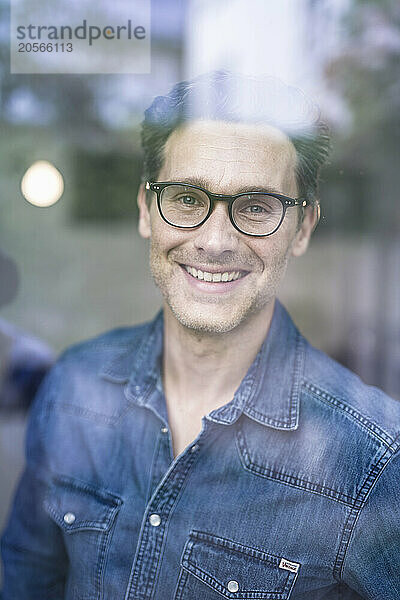 Smiling businessman wearing eyeglasses looking out through office window