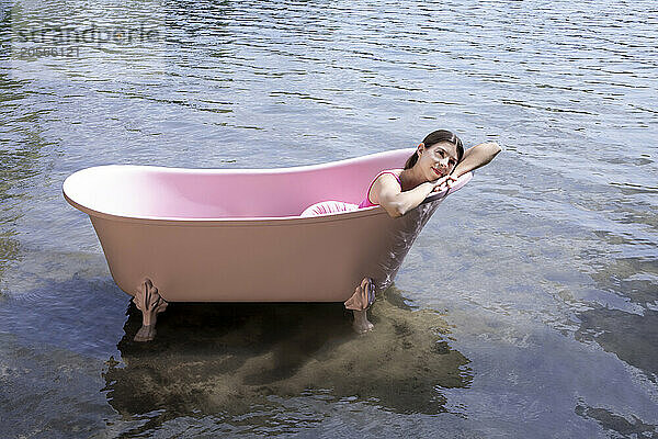 Smiling girl relaxing inside pink bathtub in lake