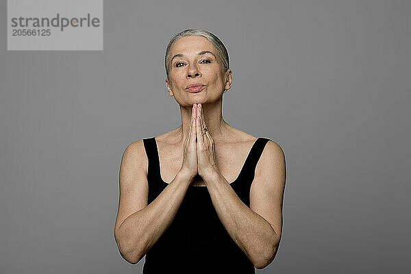 Confident senior woman with hands clasped against gray background