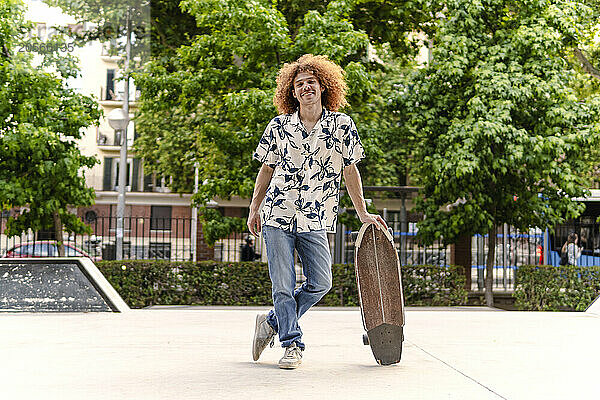 Smiling man with skateboard standing in park