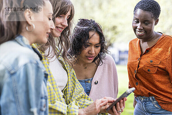 Young woman sharing smart phone with friends at park