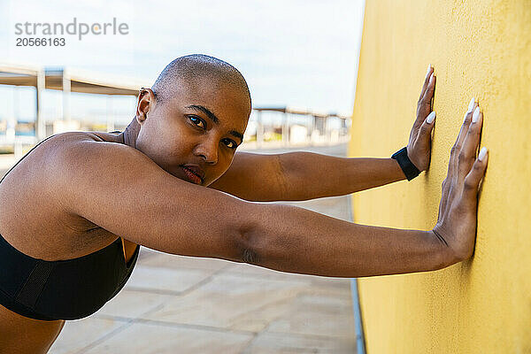 Serious bald woman doing wall push-ups on sunny day