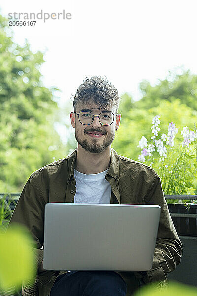 Smiling handsome young man with laptop sitting in balcony