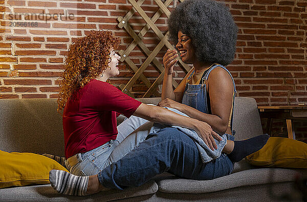 Happy multiracial friends sitting face to face on sofa at home