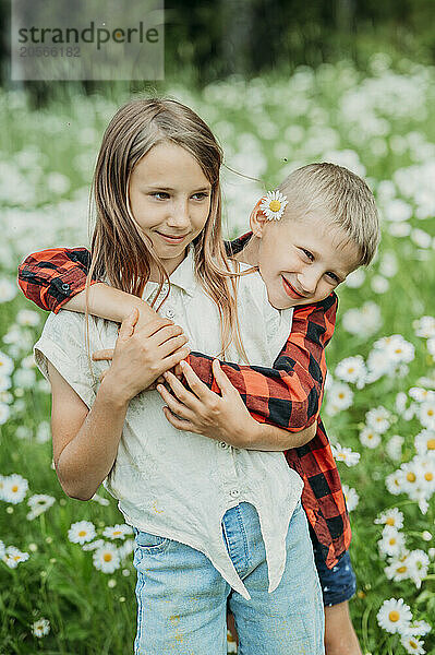 Smiling brother hugging sister from behind in daisy field