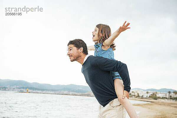 Cheerful girl with father giving piggyback ride at beach