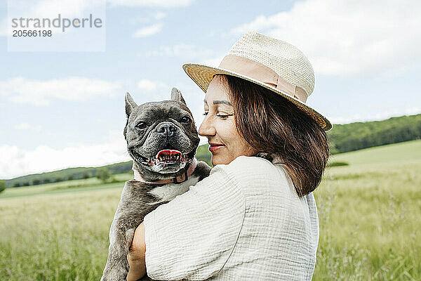 Smiling woman embracing pet french bulldog in field