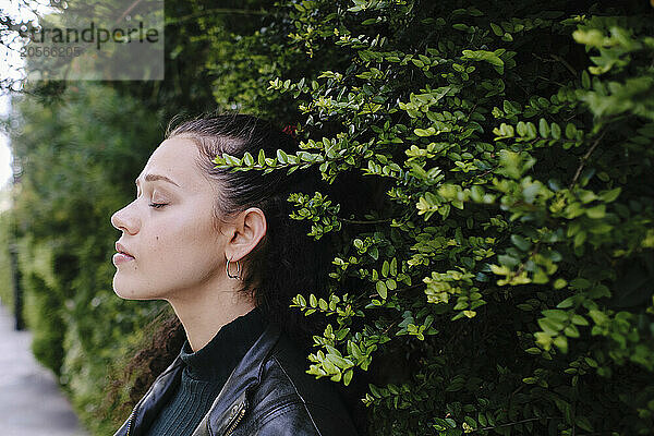 Beautiful young woman with eyes closed standing by green plants