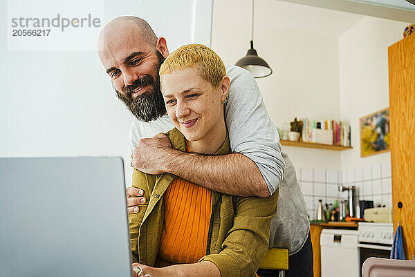 Man embracing freelancer sitting with laptop at home office