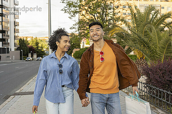 Happy young couple carrying shopping bags and walking on footpath