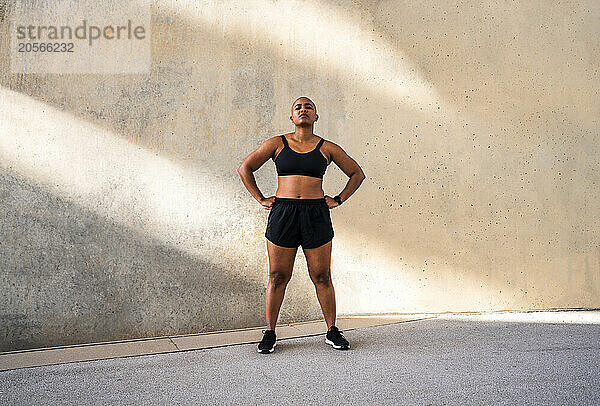 Sportive woman with muscular body standing arms akimbo in front of wall