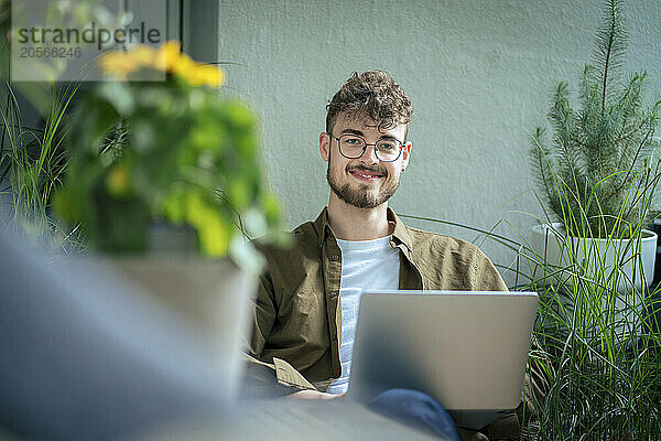 Smiling handsome young man with laptop sitting in balcony