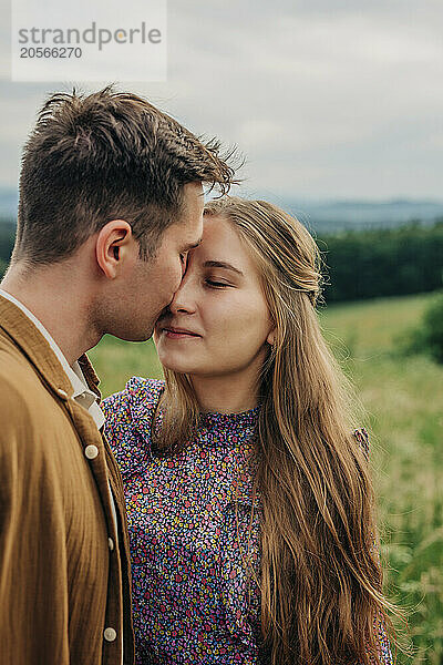 Affectionate boyfriend kissing girlfriend in meadow at mountain