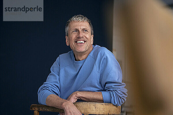 Happy senior man sitting on chair looking away at home