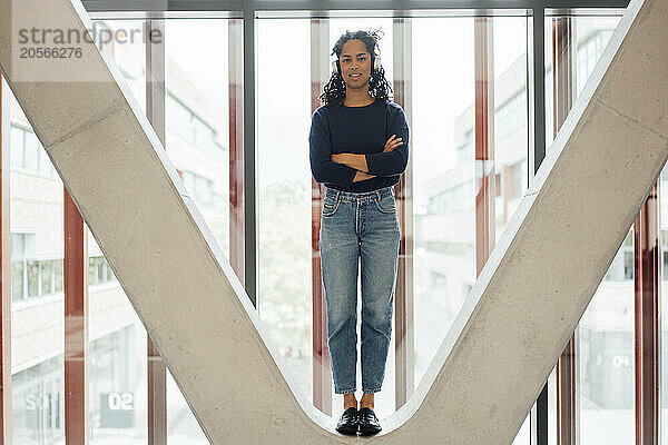 Confident young businesswoman with arms crossed standing on column at office